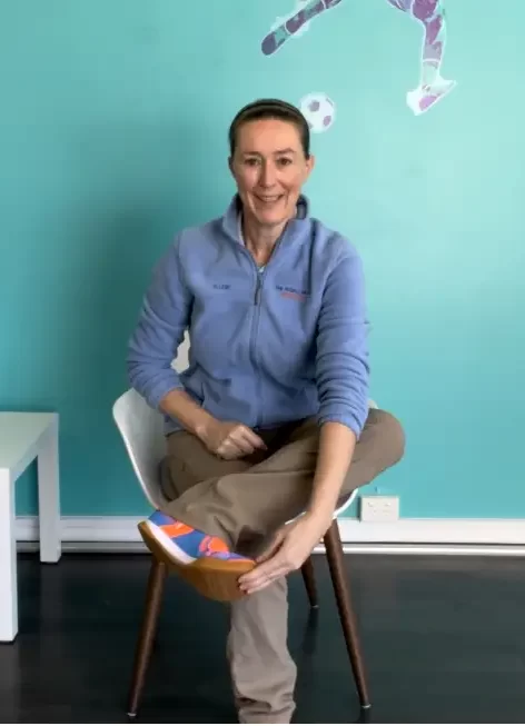 A lady smiling and sitting on a chair stretching her foot in a physiotherapy clinic.